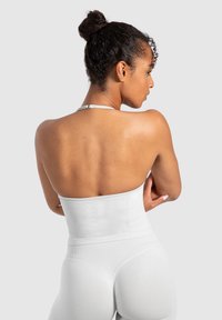 Hvid, tætsiddende tanktop med halterneck-design. Glat stof, sømløs ryg og struktureret talje for støtte, båret med matchende højtaljede leggings.
