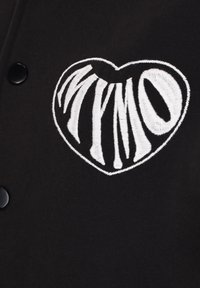 Zwarte stof met een opvallend, wit geborduurd hartontwerp met de tekst "MYMO" in een gestileerd lettertype. Inclusief zwarte knoopaccenten.