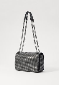 Borsa nera a forma rettangolare con catene metalliche come manici. Superficie decorata con piccoli borchiette lucide, creando un motivo testurizzato.