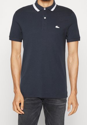 Polo-shirt marine en coton, avec un col à rayures blanches, deux boutons au cou et un petit logo blanc sur la poitrine gauche.