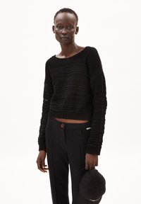 Black knitted cropped sweater with a textured stripe pattern, paired with black trousers featuring a brown button and pockets.
