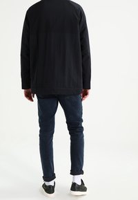 Černá lehká bunda s texturovaným povrchem, spárovaná s tmavě modrými džíny. Bílé kotníkové ponožky a černé tenisky dotvářejí outfit.