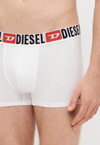 Baltas bokseršorti ar melnu un sarkanu Diesel logotipa jostiņu; mīksts kokvilnas materiāls, pieguļošs dizains un gluda tekstūra.