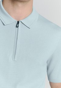 Lichtblauwe polo met korte mouwen, gemaakt van zacht breimateriaal, met een ritssluiting bij de hals en een klassiek kraagontwerp.