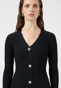 Μαύρο ριμπ πουλόβερ με V-λαιμόκοψη, διακοσμημένο με ασημί κουμπιά και μακριά μανίκια, με ομοιόμορφη υφή σε όλο το ύφασμα.