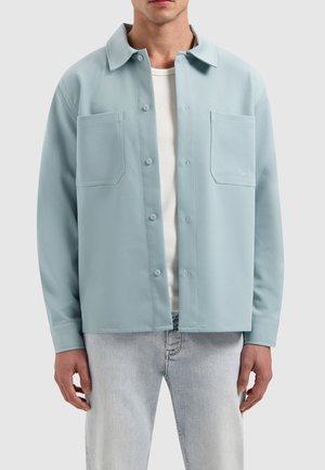 Lichtblauwe shirtjacket met een kraag, twee voorzakken, knoopsluiting en een gladde textuur, gedragen over een wit onderhemd.