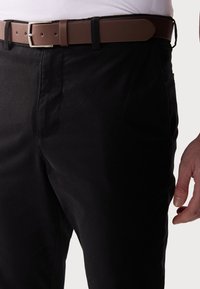 Svart byxor med en slät textur, med ett brunt bälte med en silverfärgad spänne. Byxorna har diskret sömnad och sidfickor.