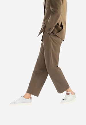 Completo beige su misura con pantaloni larghi, abbinato a sneakers bianche con tocchi di grigio chiaro e una linguetta in pelle marrone.