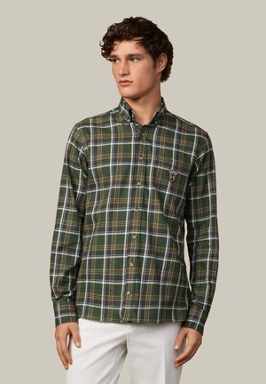 Camisa de cuadros verdes con detalles en blanco y marrón, cuello abotonado, mangas largas y un parche con logo en el pecho, tejido texturizado.