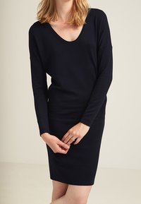 Abito lungo blu navy a maniche lunghe con scollatura a V profonda e silhouette aderente. Tessuto morbido, texture liscia e design minimalista.