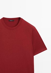 T-shirt rouge uni à manches courtes avec col rond surpiqué et étiquette de marque visible à l'intérieur du col.