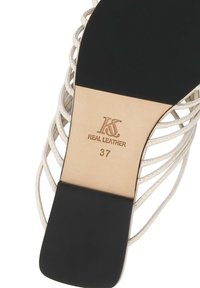 Σόλα σανδάλου με μαύρο τακούνι, μπεζ δερμάτινη εσωτερική σόλα με σήμανση "KS Real Leather 37" και λευκό επάνω μέρος με λουράκια που φαίνεται γύρω από τις άκρες.