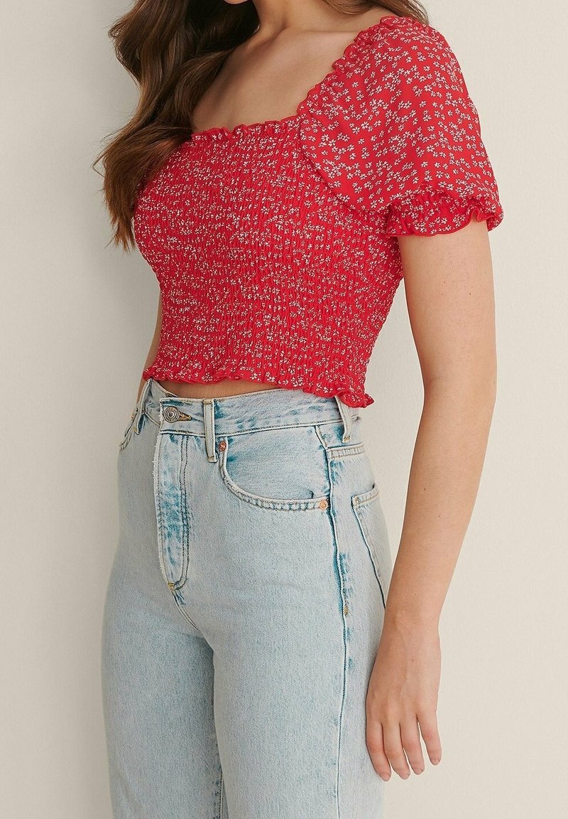 Rotes Blumenmuster-Cropped-Top mit geraffter Textur und kurzen Puffärmeln, kombiniert mit hellblauen hoch-taillierten Jeans mit klassischen Taschen.