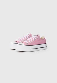 Pink canvas sneakers with white laces, black side stripes, and a textured white rubber sole. Features a round toe design and logo on tongue.