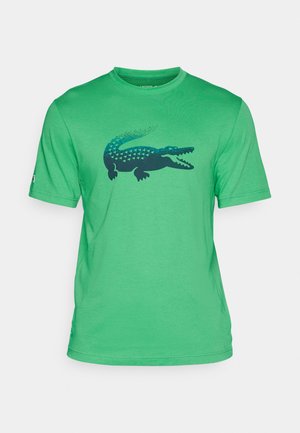 Zelena majica s kratkim rukavima izrađena od mekanog materijala, s grafičkim dizajnom tamnoplavog krokodila na prednjoj strani. Klasičan stil s okruglim izrezom.