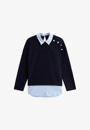 Haut à manches longues bleu marine superposé sur une chemise rayée bleue et blanche avec col pointu, comportant quatre boutons en argent sur l'épaule droite.