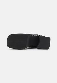 Sandale en cuir noir avec une semelle en caoutchouc texturé, dotée d'une sangle réglable avec boucle et d'un petit talon épais pour plus de stabilité.