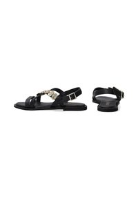 Schwarze Leder-Sandalen mit flachem Design, mehreren Riemen und einem dekorativen Metallakzent sowie einem Schnallenverschluss am Knöchel.