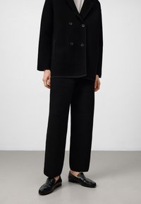 Veste noire à double boutonnage côtelée avec de grands boutons, assortie à un pantalon côtelé. Portée avec des chaussures noires à enfiler.