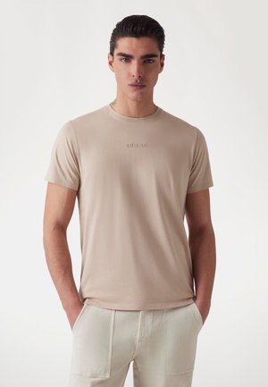 Beige short-sleeve t-shirt made of soft cotton with a crew neckline and embroidered "GUESS" logo on the chest. Smooth texture.