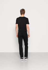 T-shirt nera abbinata a pantaloni neri. I pantaloni presentano una vestibilità classica e tasche posteriori discrete. Il modello indossa sneakers bianche e nere.