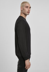 Svart hettegenser laget av mykt materiale, med lange ermer, rund hals og ribbede mansjetter. Enkelt design med en avslappet passform.