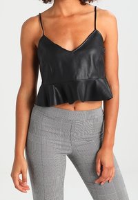 Svart faux läder crop top med V-ringning och spagettistroppar, med en utsvängd peplumkant. Kombinerad med grå rutiga tajta byxor.