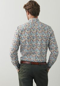 Pitkähihaine paita kevyestä kankaasta, jossa on monivärinen kukkakuosi valkoisella taustalla. Sisältää terävän kauluksen ja slim fit -leikkauksen.