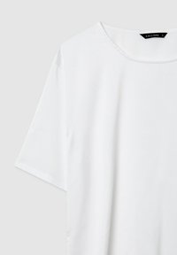 T-shirt bianco a maniche corte con scollatura tonda, realizzato in tessuto liscio. Presenta cuciture sottili ai lati e un'etichetta del brand sul collo.