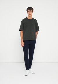 T-shirt oversize grigio scuro a maniche corte, abbinata a pantaloni slim-fit blu navy e sneakers bianche su uno sfondo neutro.