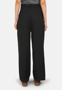 Black wide-leg trousers made of smooth fabric, featuring two back pockets and a high waist. Complements with brown footwear.