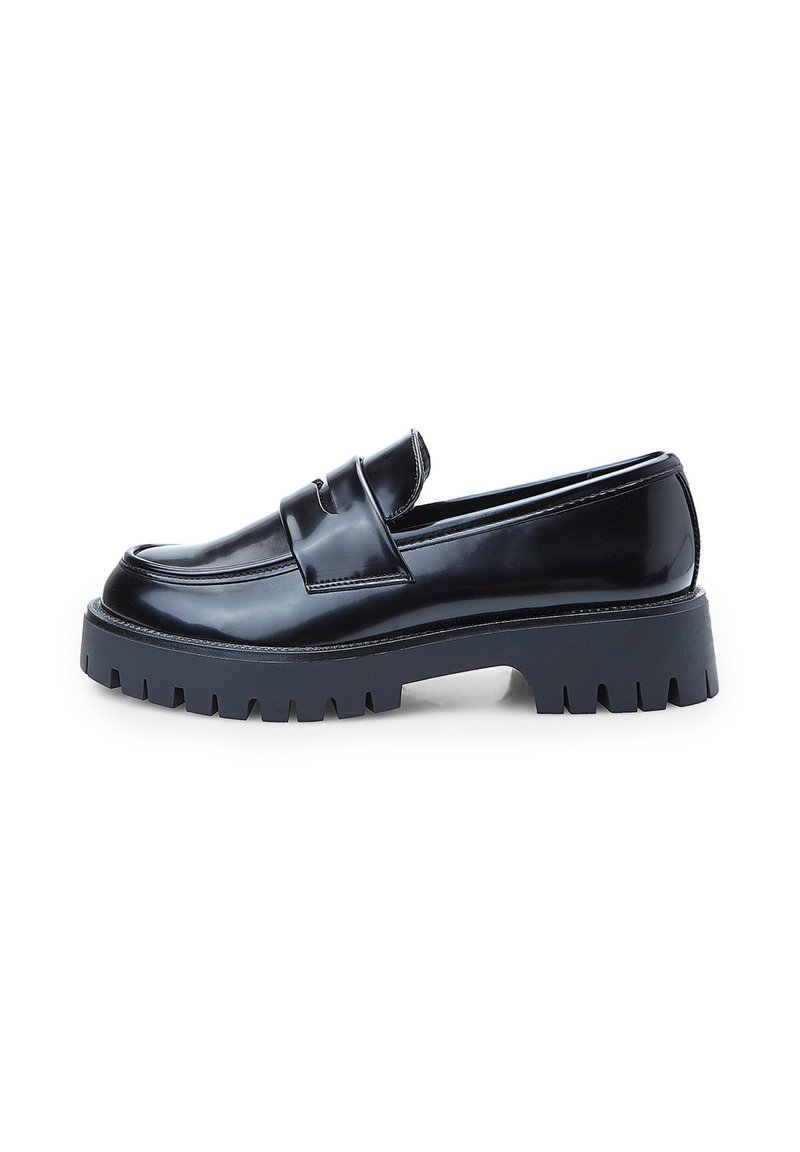 Mocasines de charol negro con una suela de goma gris gruesa, que presentan una cinta decorativa y costuras definidas a lo largo de los bordes.