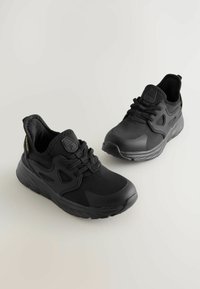 Baskets de sport noires en matériau synthétique, avec un design épuré, des accents texturés et une semelle rembourrée avec un motif de traction prononcé.