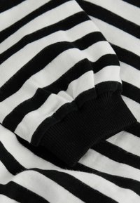 Gros plan sur une manche en tissu rayé noir et blanc avec un poignet noir côtelé, montrant une texture douce et les détails du motif.