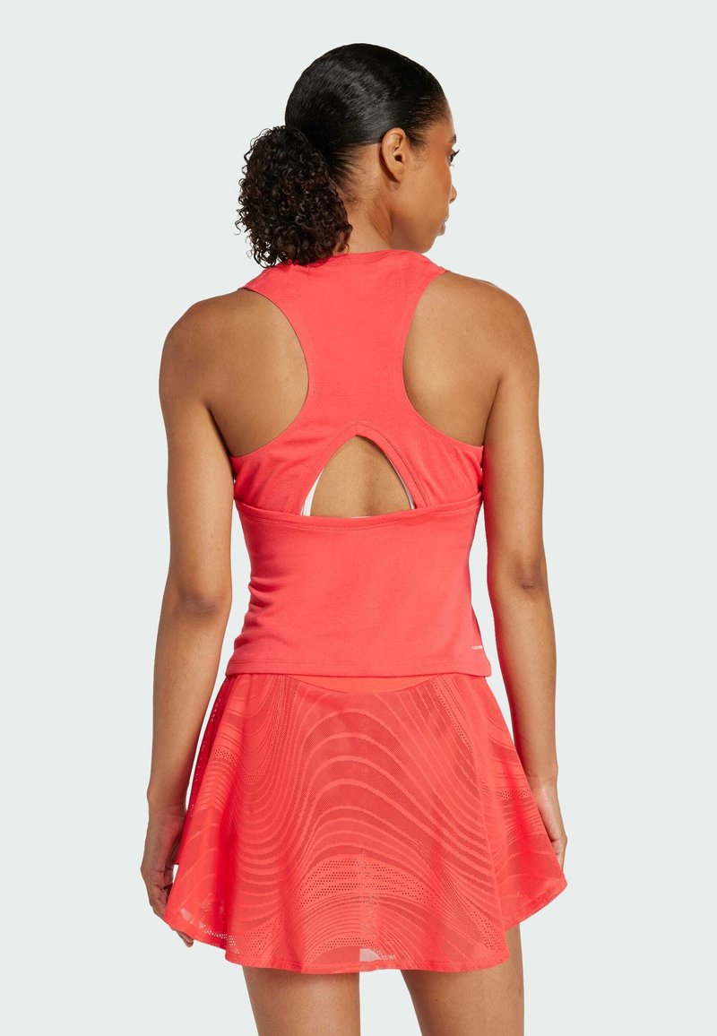 Débardeur de sport rouge avec un dos en œillet, associé à une jupe superposée assortie présentant un motif ondulé et un tissu léger et respirant.