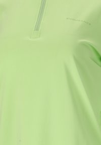 T-shirt de sport vert clair avec une courte fermeture éclair et le texte « ENDURANCE » sur la partie supérieure de la poitrine.