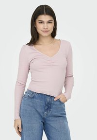 Langærmet lyserød ribbet top med V-hals, med gatherdetaljer foran og bølget kant, parret med højtaljede blå jeans.