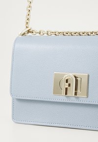 Borsa a spalla in pelle azzurro chiaro con superficie testurizzata. Presenta una chiusura e una tracolla in tono dorato, con un design rettangolare elegante.