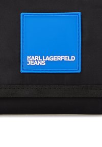 Čierny textilný púch s modrým obdĺžnikovým logom. Na logu je v bielych embosovaných písmenách napísané "KARL LAGERFELD JEANS".