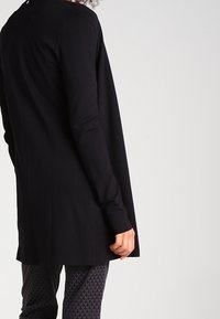 Czarny longsleeve z luźnym krojem, wykonany z miękkiego materiału, charakteryzujący się prostym wzorem i delikatną fakturą. Widok z tyłu.