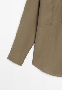 Khaki long-sleeve shirt, textured fabric, curved hem, buttoned cuff, featuring subtle stitching details, and a smooth finish.