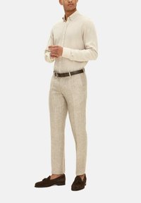 Beige linnen overhemd met kraag, gecombineerd met lichtbeige broeken en donkerbruine suède instappers. Eenvoudig ontwerp, op maat gemaakt pasvorm.