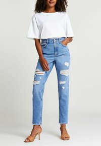 Jeansy z wysokim stanem z niebieskiego denimu z przetarciami, prostym krojem nogawki i postrzępionymi brzegami, w połączeniu z luźną białą koszulką bawełnianą.