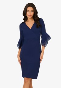Robe bleu marine à design enveloppant, avec des manches cloches superposées et transparentes, et une silhouette ajustée qui arrive au genou.