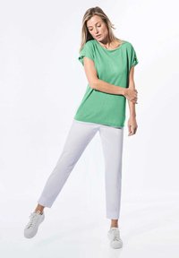 Grünes kurzärmliges Oberteil aus weichem Stoff, kombiniert mit weißen Slim-Fit-Hosen. Das Outfit wird durch weiße Sneaker ergänzt. Schlichtes und lässiges Design.