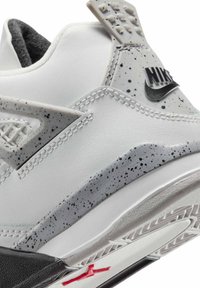 Sneaker Nike avec une tige synthétique blanche, des accents gris mouchetés, un talon noir texturé et un logo rouge sur la semelle extérieure. Présente un design unique.