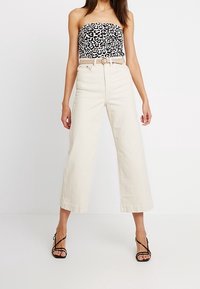 Top senza spalline con stampa leopardata in bianco e nero abbinato a pantaloni a vita alta e gamba larga di colore crema e sandali neri con lacci.