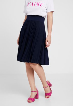 Navy pleated skirt with a wide waistband, paired with pink strappy heeled sandals. The fabric appears soft with a flowing design.