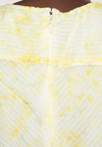 Gult och vitt randigt tyg med blommönster, med en dragkedja bak. Mjukt, lätt material med en lätt strukturerad yta.