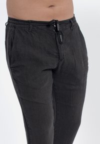 Pantaloni neri in lino con vita regolabile, dotati di due tasche laterali e una vestibilità morbida, texture liscia, adatti per un abbigliamento casual.
